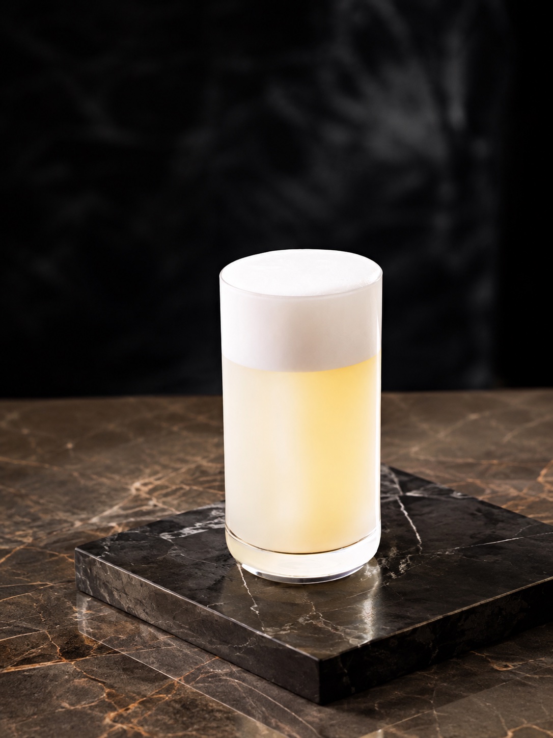 Silver Gin Fizz in a highball glass with a tall, light foam crown on black marble